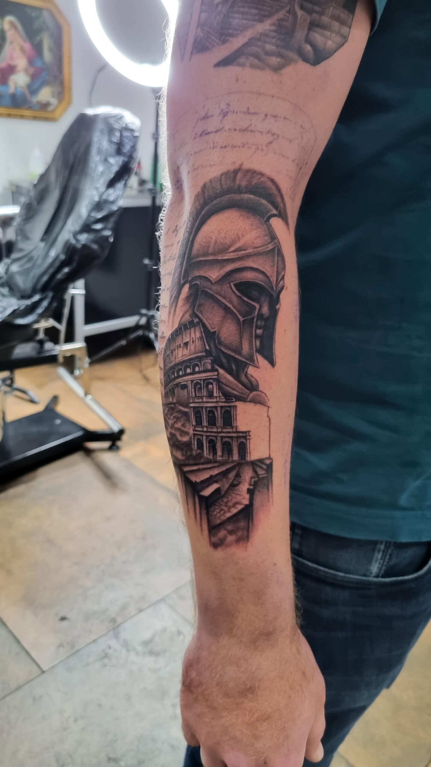 Tätowierter Arm mit römischem Helm und Kolosseum, schwarzes T-Shirt, interessanter Hintergrund.