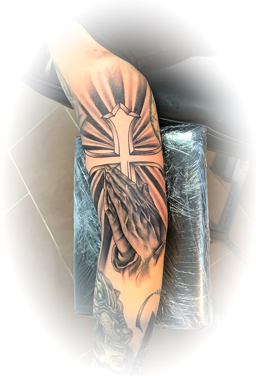 Tätowierter Arm mit Kreuz und betenden Händen, schwarz-graue Tinte, kunstvoller Stil.