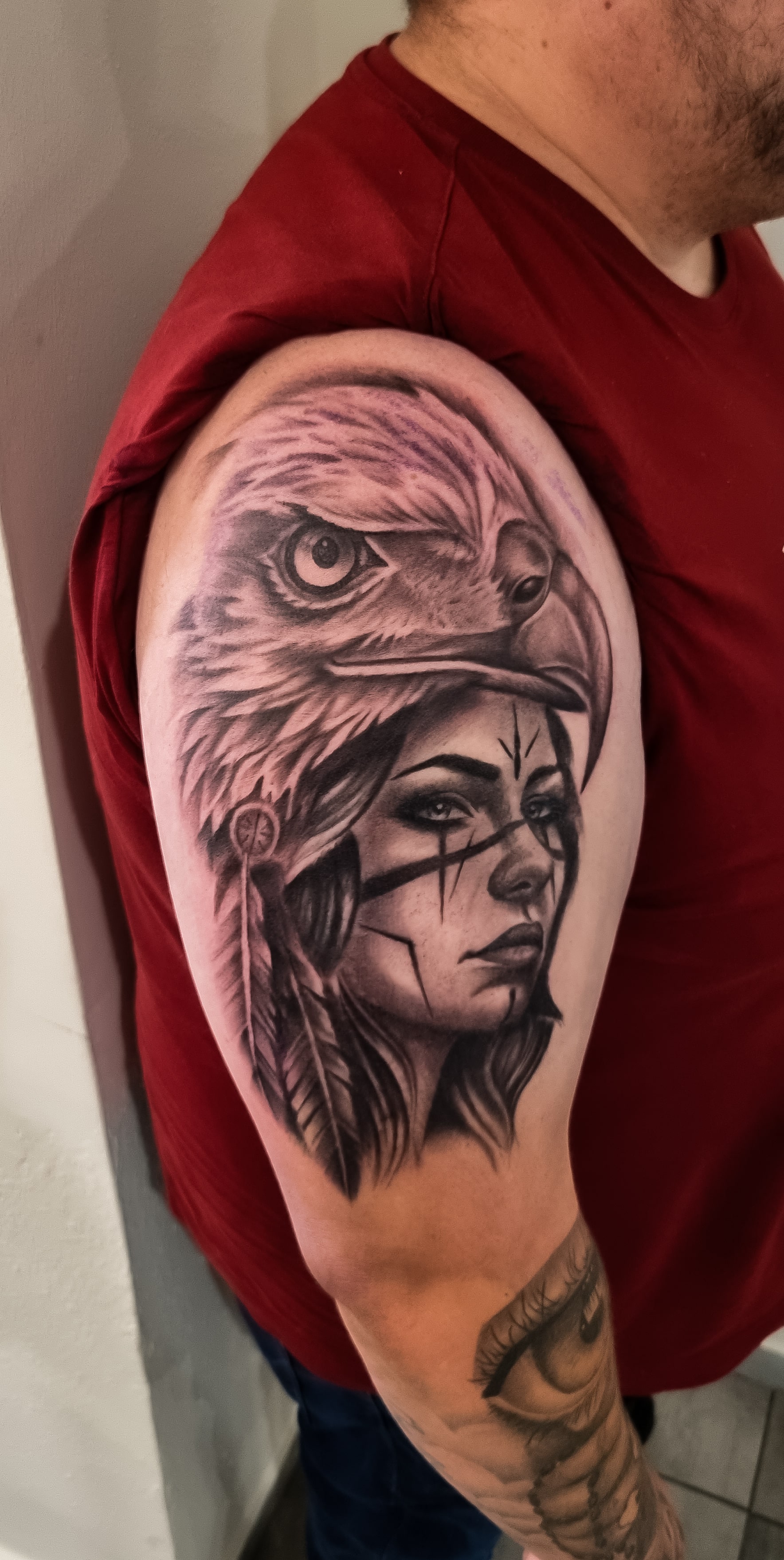 Ein Mann mit rotem Hemd hat ein detailliertes Tattoo von einer Frau mit Adler.