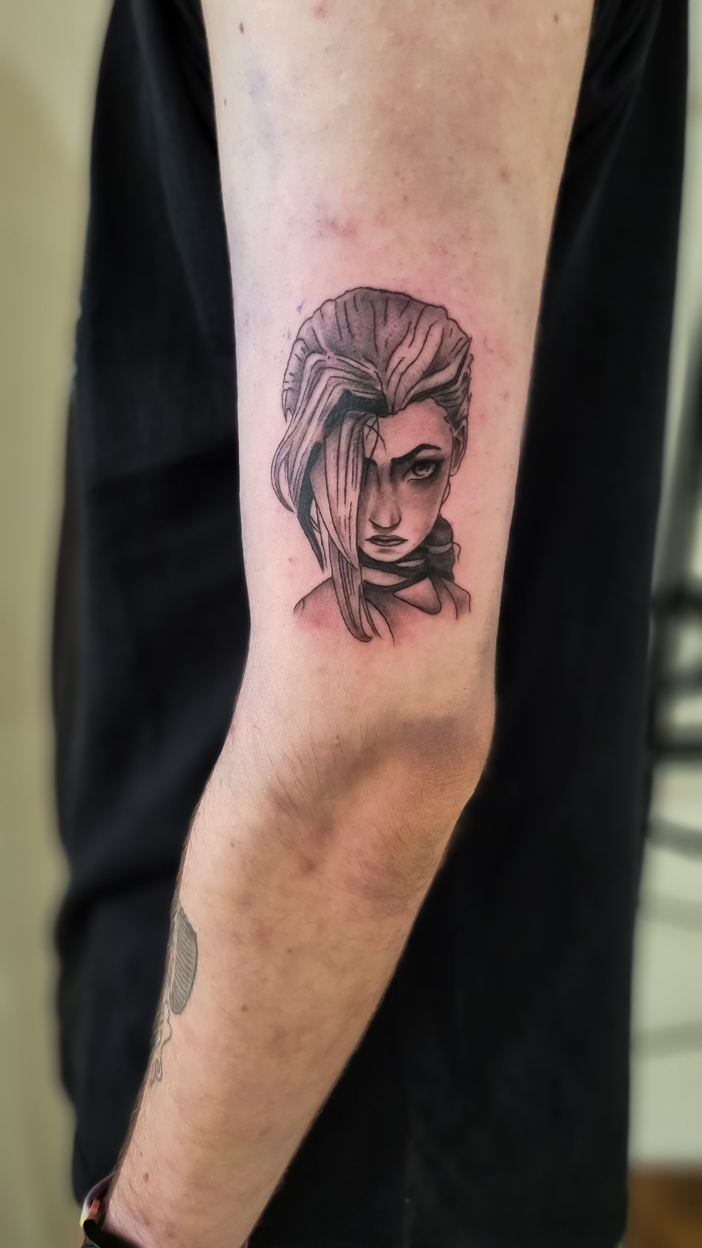 Ein Tattoo mit einer ausdrucksstarken Frau mit Haaren im Gesicht auf einem Arm.