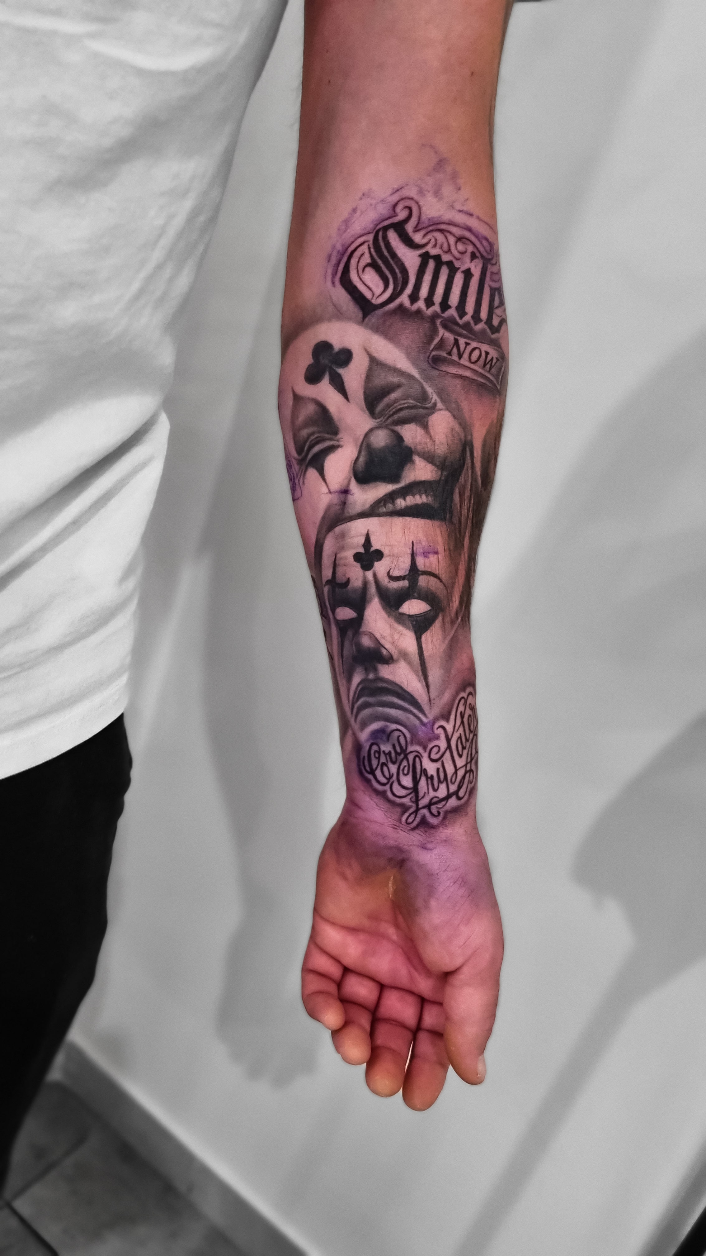 Ein Arm mit einem farbigen Tattoo von Masken, Rosen und gotischen Buchstaben.