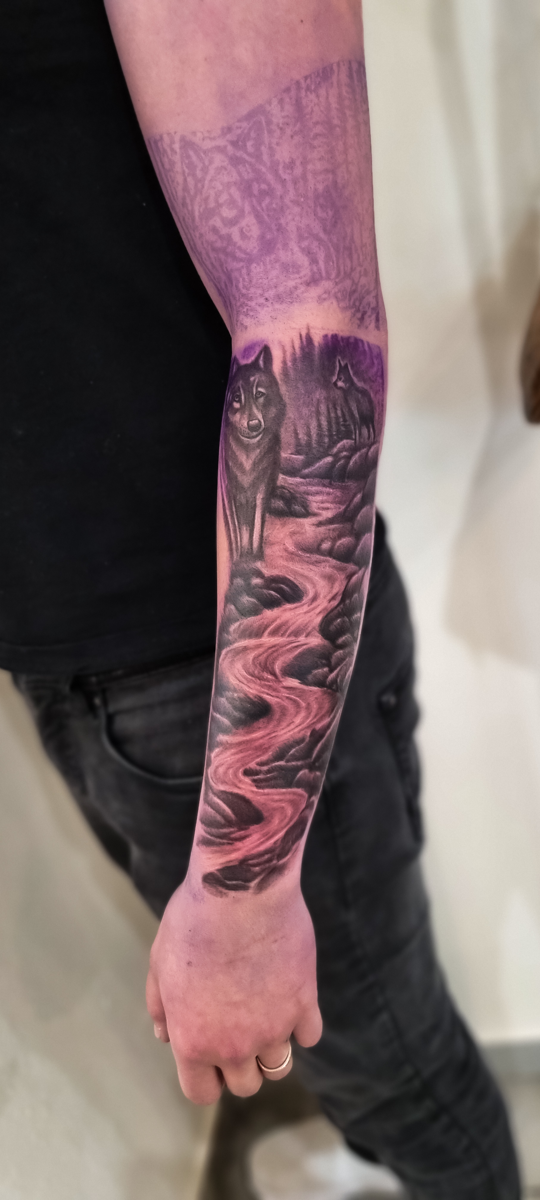 Ein Arm mit einem detaillierten Tattoo von zwei Wölfen an einem Fluss in Schwarzlila