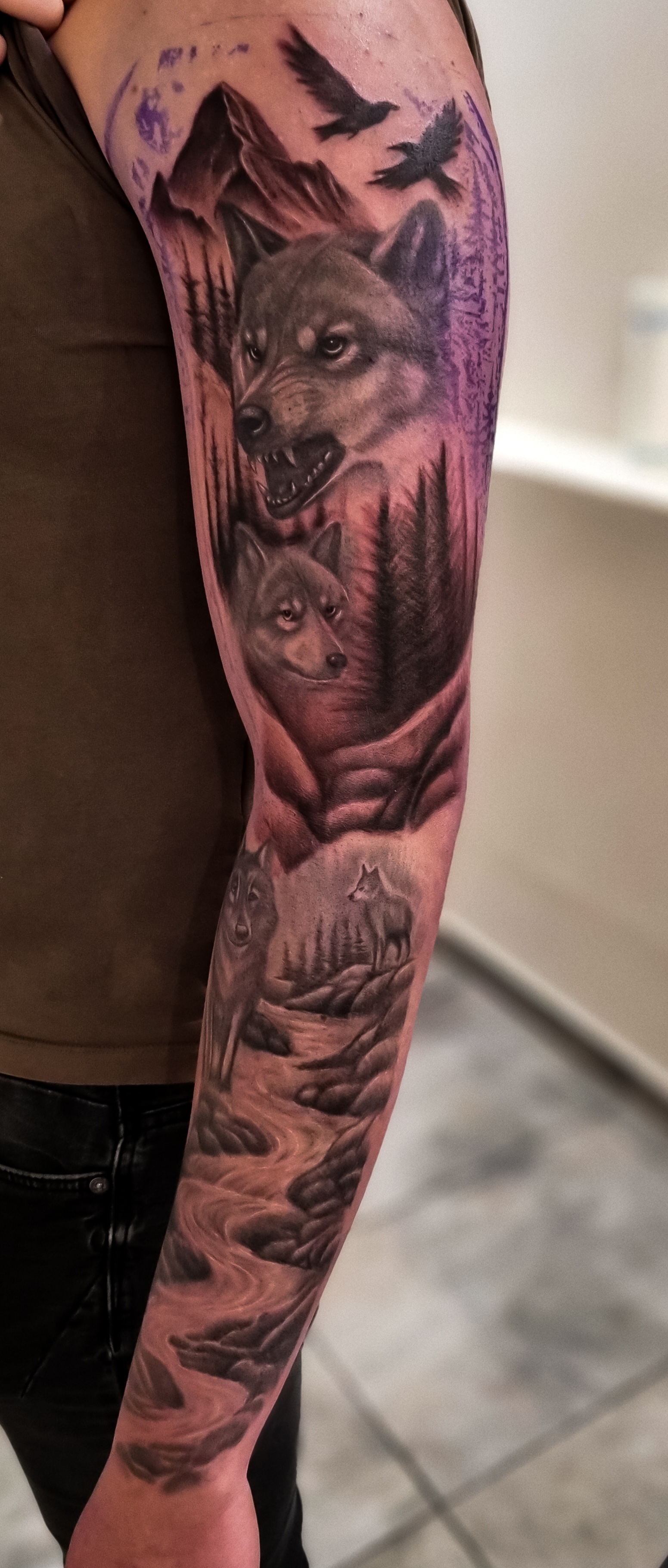 Eine tätowierte Männerarm mit detailreichen Wölfen, Bäumen und Bergen in Schwarzgrau